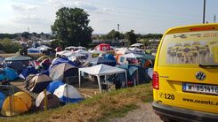 Ein gelbes ÖAMTC Pannenfahrzeug steht neben mehreren Zelten auf einem Campingplatz in der Natur.