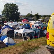 Ein gelbes ÖAMTC Pannenfahrzeug steht neben mehreren Zelten auf einem Campingplatz in der Natur.