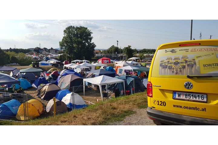 Ein gelbes ÖAMTC Pannenfahrzeug steht neben mehreren Zelten auf einem Campingplatz in der Natur.