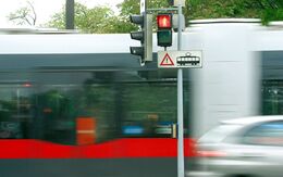 Eine Fußgängerampel steht auf rot. Im Hintergrund fährt eine rote Straßenbahn und ein graues Auto vorbei.