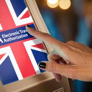 Ein Bildschirm, der eine britische Flagge mit dem Schrifzug ETA Electronic Travel Authorization zeigt, und eine Hand, die den Bildschirm berührt