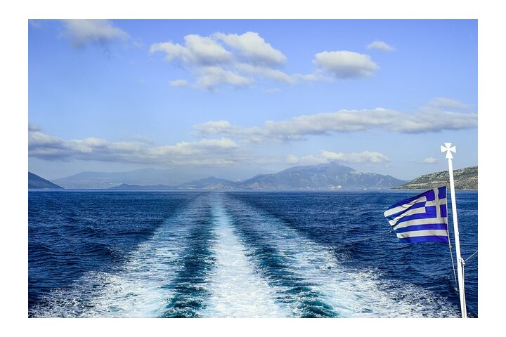 Blick von einer Fähre auf griechische Inseln in der Ferne, mit einer im Wind wehenden griechischen Flagge im Vordergrund