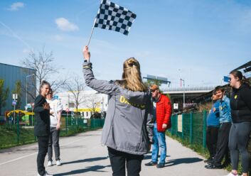 Man sieht eine Frau, die eine schwarz-weiß karierte Fahne schwenkt. neben ihr stehen Menschen