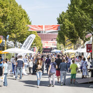 Viele Messebesucherinnen und Besucher im Freigelände einer Messe unterwegs.