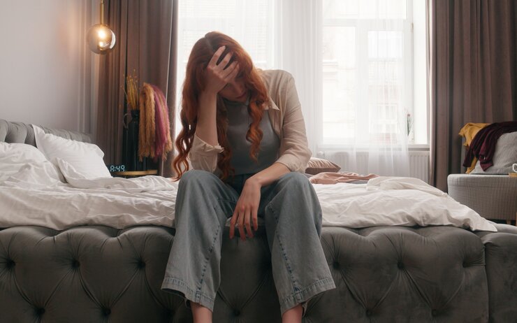 Hotelmängel am Urlaubsort Verzweifelte Frau sitzt auf einem Bett in einem Zimmer und sieht frustriert aus.