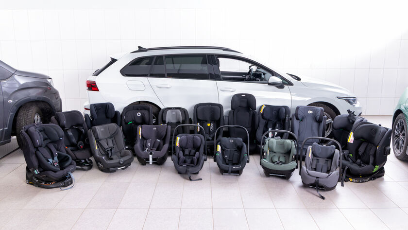 16 Kindersitze stehen nebeneinander am Boden vor einem weißen Auto 