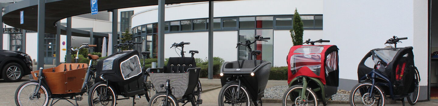 Sechs einspurige Elektro-Lastenfahrräder sind vor einem Gebäude aufgestellt.