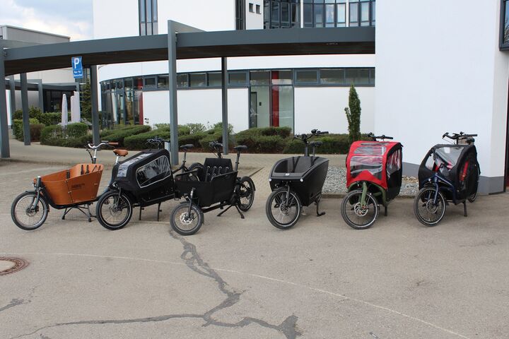 5 einspurige E-Lastenfahrräder stehen vor Haus.