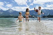 Drei kleine Kinder planschen im See, im Hintergrund die Bergkulisse.
