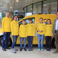 Vier Kinder in gelben ÖAMTC-Trikots stehen neben drei Erwachsenen vor einem ÖAMTC Pannenfahrzeug