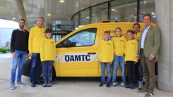 Vier Kinder in gelben ÖAMTC-Trikots stehen neben vier Erwachsenen vor einem ÖAMTC Pannenfahrzeug