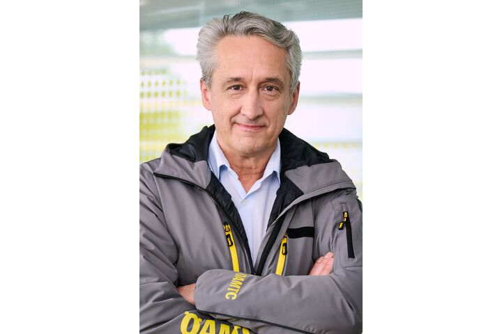 Das Bild ist ein Portrait von Steffan Kerbl, der frontal in die Kamera schaut, eine graue Jacke mit gelber ÖAMTC-Aufschrift trägt und die Arme verschränkt.