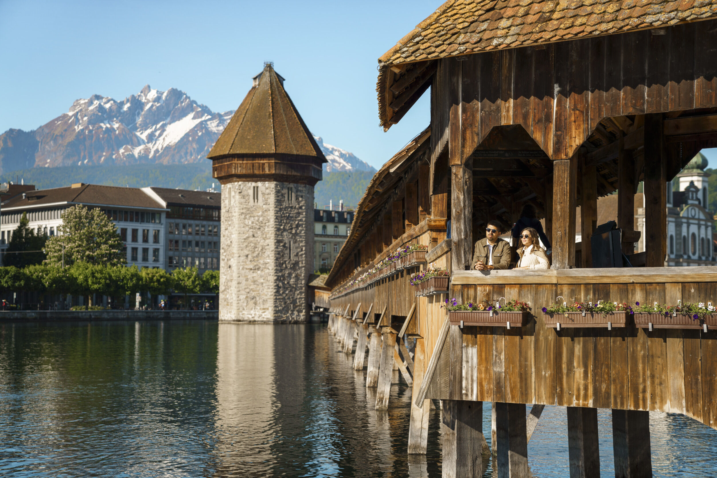 Ein Paar steht auf der Kapellbrücke in Luzern, Schweiz, mit den Alpen im Hintergrund.