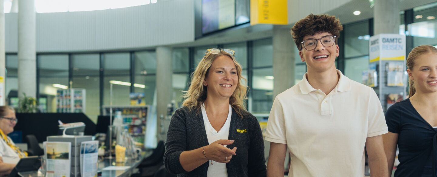Karriere_Header_Schueler_innen.jpg Drei Personen gehen durch den Schalterbereich eines ÖAMTC Stützpunktes. Links eine erwachsene Frau in Dienstkleidung, die den beiden Jugendlichen (ein junger Mann und eine junge Frau) etwas zeigt.