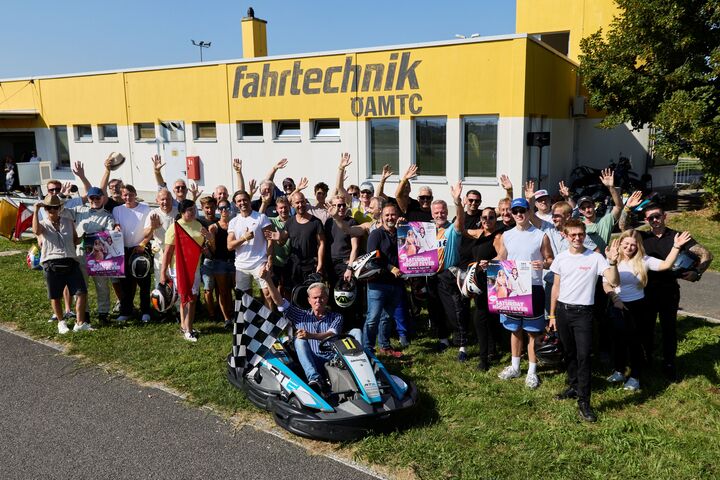 Das Ensemble der Seefestspiele Mörbisch posiert für ein spaßiges Gruppenbild vor der Boxengassengasse der Kartstrecke