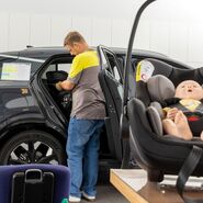 Im Vordergrund liegt eine Puppe in einem Kindersitz, im Hintergrund bereitet ein Mann in ÖAMTC-Kleidung alles für den Test im Auto vor.
