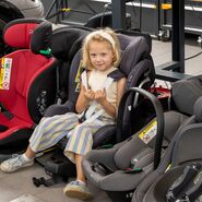 Eines der Testkinder posiert für ein Foto, während es in einem Kindersitz sitzt.