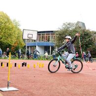 Ein Kind hält in der linken Hand eine angebundene Kette, während es einhändig Fahrrad fährt