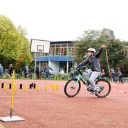Ein Kind hält in der linken Hand eine angebundene Kette, während es einhändig Fahrrad fährt
