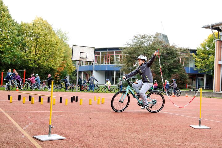 Ein Kind hält in der linken Hand eine angebundene Kette, während es einhändig Fahrrad fährt