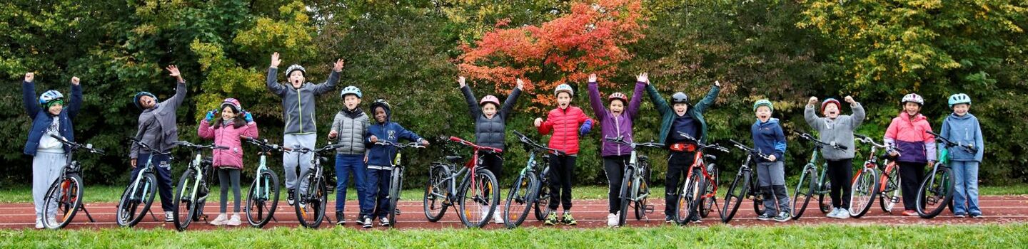 Vierzehner Kinder mit Fahrrad und Helm stehen aufgereiht nebeneinander und jubeln fröhlich.