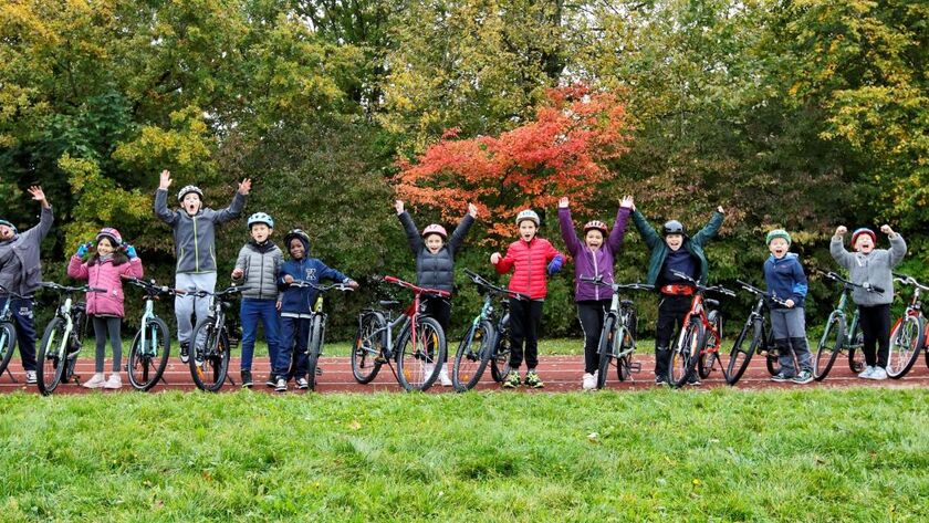 Vierzehner Kinder mit Fahrrad und Helm stehen aufgereiht nebeneinander und jubeln fröhlich.