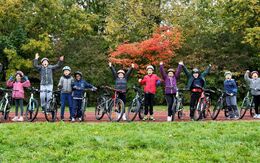 Vierzehner Kinder mit Fahrrad und Helm stehen aufgereiht nebeneinander und jubeln fröhlich.