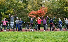 Vierzehner Kinder mit Fahrrad und Helm stehen aufgereiht nebeneinander und jubeln fröhlich.