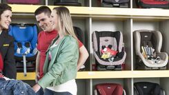 ÖAMTC-Mitarbeiterin zeigt Eltern mit Kind einen Kindersitz und erklärt die Sicherheitsmerkmale sowie die richtige Installation für den optimalen Schutz von Kindern im Auto.