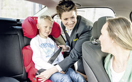 ÖAMTC-Mitarbeiterin erklärt einer Mutter, wie man ein Kind sicher im Kindersitz anschnallt, während sie die richtigen Sicherheitsvorkehrungen demonstriert.