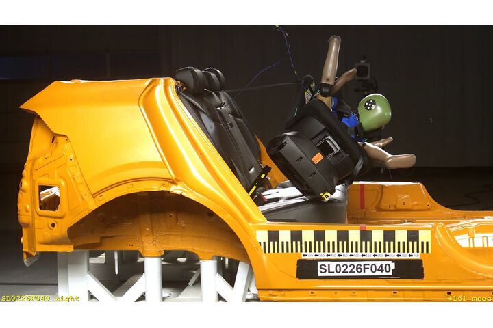 Das Bild zeigt einen Kindersitztest, dabei wird der Kindersitz, indem ein Dummie sitzt, aus der Basishalterung geschleudert. 