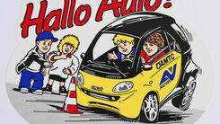 Logo des Verkehrserziehungsprogramms. Zwei Kinder stehen am Straßenrand und beobachten das ÖAMTC Hallo Auto-Auto bei einer Vollbremsung vo einem Verkehrshütchen. Im Auto eine angegurtete Erwachsene als Fahrerin. Am Nebensitz ein weiteres, ebenfalls angegurtetes Kind. Am Auto ist neben dem ÖAMTC Logo auch das AUVA Logo zu sehen.