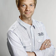 Porträtfoto eines blonden kurzhaarigen Mannes mittleren Alters mit verschränkten Armen in einem grauen Hemd