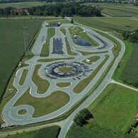 ÖAMTC Fahrtechnik Zentrum Lang/Lebring Inmitten einer ländlichen Landschaft erstreckt sich das Fahrtechnik Zentrum Lang/Lebring. Es gibt viele asphaltierte Trainingsstrecken mit Kreuzungselementen, Kreisbahn und Kurvenkombinationen. Im Hintergrund ist ein Gebäude.