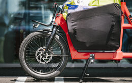 Rotes Lastenfahrrad im Vordergrund, Auto verschwommen im Hintergrund.