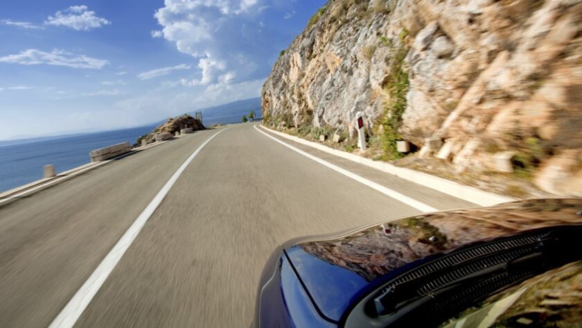 Ein Auto fährt entlang einer Küstenstraße mit einer steilen Felswand auf der rechten Seite.