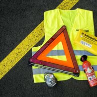 Pflichtausstattung für Autofahrer auf dem Boden eines Parkplatzes ausgelegt: Warnweste, Warndreieck, Verbandszeug und Ersatzlampenset