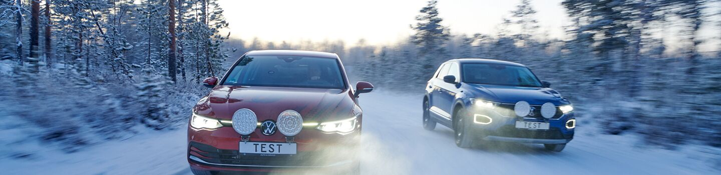 2 Autos fahren auf schneebedeckter Fahrbahn in Winterlandschaft, am Kennzeichen der beiden Autos steht Test.