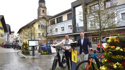 Landesdirektorin Martina Schlegel-Lanz und Vizebürgermeister Rupert Freundlinger mit zwei Fahrrädern an der neuen Self-Service Station, Kirchturm von Seekirchen am Wallersee im Hintergrund