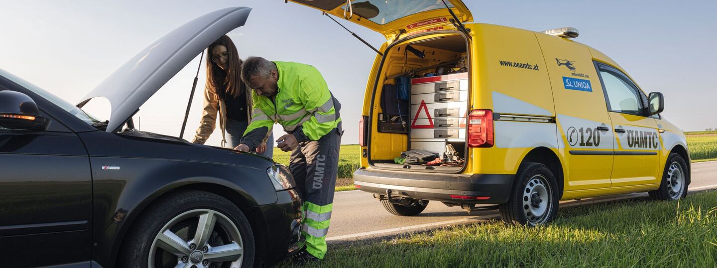 Pannenfahrer mit einer weiblichen Person vor geöffneter Motorhaube
