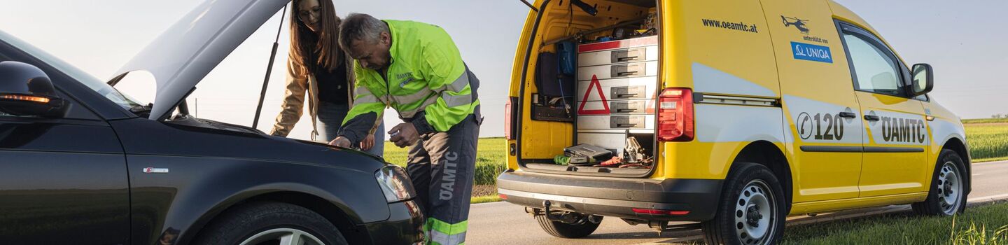 Pannenfahrer mit einer weiblichen Person vor geöffneter Motorhaube