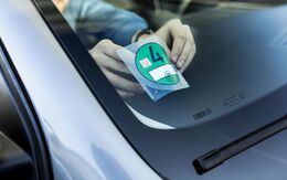 Ein Mensch klebt gerade eine Umweltplakette auf die Innenseite der Autofrontscheibe .