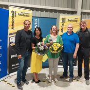 Im Bild zu sehen sind die drei Erstplatzieren des Tarocktuniers in der Mitte mit Blumen und Gutscheinen in der Hand, links und rechts Gratulanten der Veranstaltungsorganisation, im Hintergrund sind man Roll-Ups der Sponsoren.