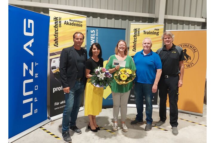 Im Bild zu sehen sind die drei Erstplatzieren des Tarocktuniers in der Mitte mit Blumen und Gutscheinen in der Hand, links und rechts Gratulanten der Veranstaltungsorganisation, im Hintergrund sind man Roll-Ups der Sponsoren.
