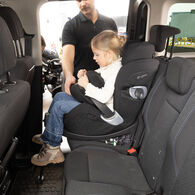 OEAMTC-Kindersitztest-Fruehjahr-2025 (6) Ein kleines Mädchen mit blonden Haaren sitzt im Rahmen des Kindersitztests in einem Kindersitz auf der Rückbank eines Autos. Sie ist von der Seite zu sehen, im Hintergrund ein ÖAMTC-Techniker.