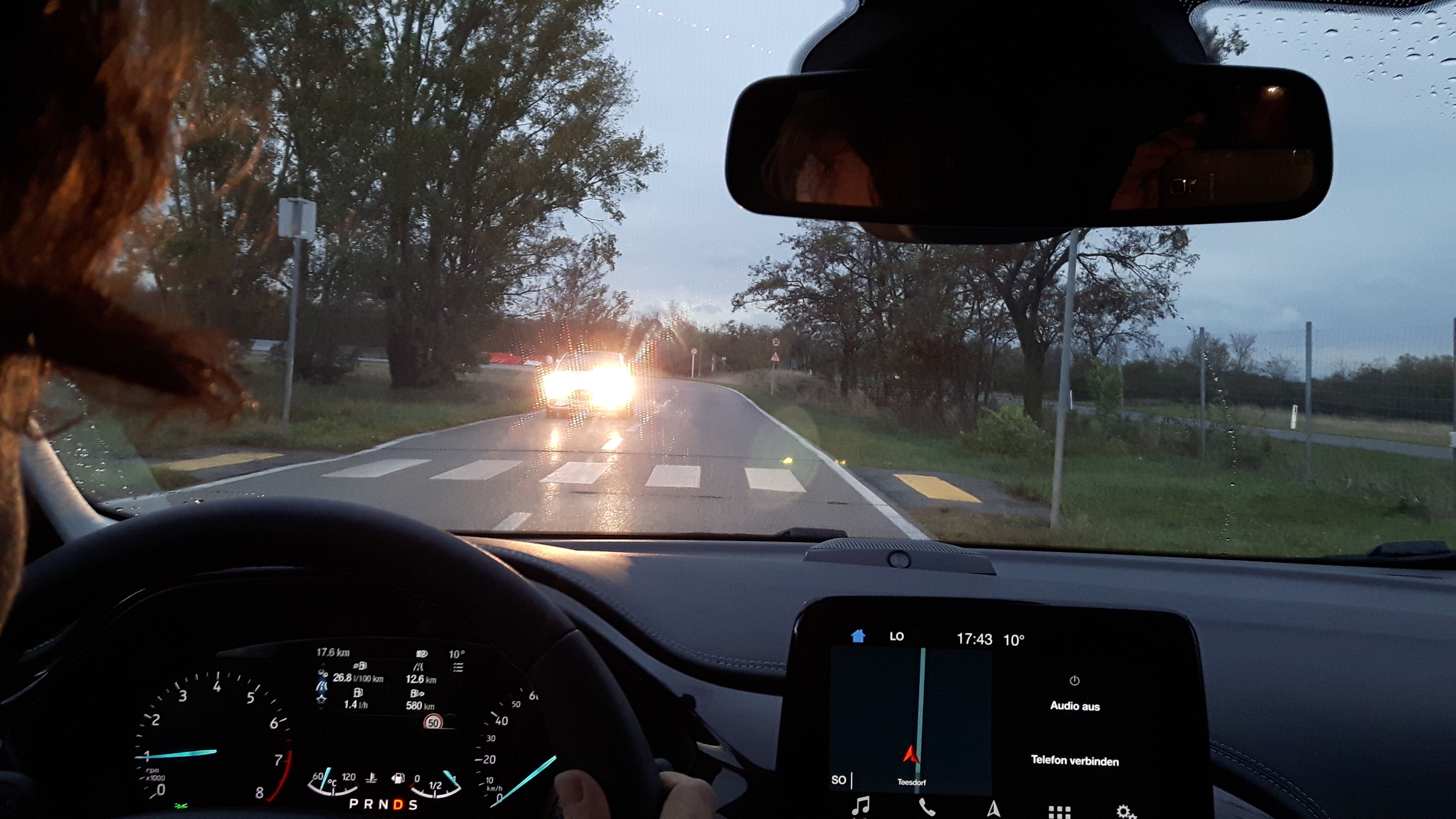 Blick aus dem Cockpit auf entgegenkommendes Auto, das den Scheinwerfer voll aufgeblendet hat.