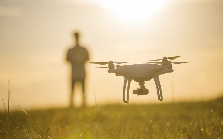 Eine fliegende Drohne über einer Wiese im Sonnenuntergang. Im Hintergrund, unscharf, eine Person.