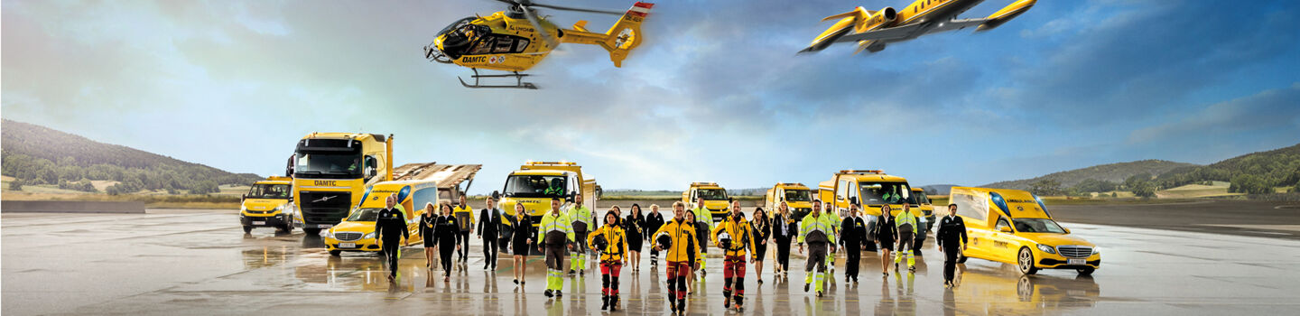 Eine Flotte von gelben Rettungsfahrzeugen und Luftfahrzeugen steht auf einem Flugfeld. Zu sehen ein Krankenwagen, Pannenfahrzeuge, ein Abschlepp-LKW, ein Rettungshubschrauber in der Luft sowie ein Ambulanzflugzeug. Davor stehen Einsatzkräfte in leuchtender Schutzkleidung. 