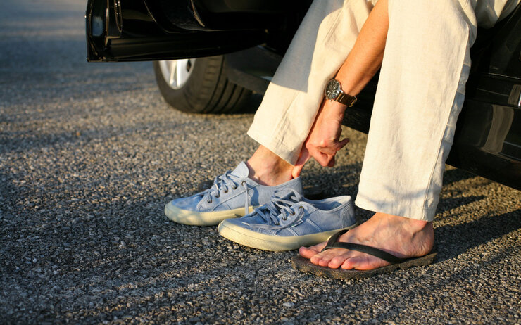 Person wechselt Flip-Flops gegen ein Paar geschlossene, bequeme Sportschuhe.