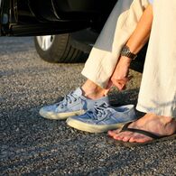 Eine Person wechselt im Auto sitzend ihre Schuhe von Flip-Flops zu bequemen und festen Straßenschuhen